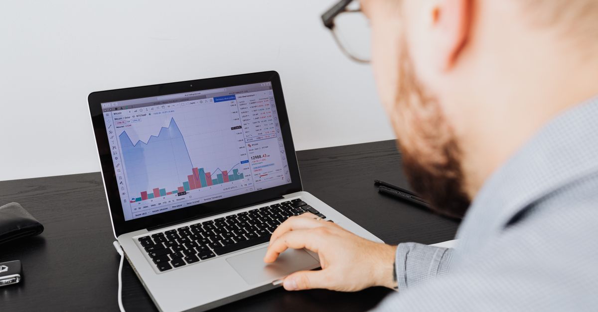 An analyst studying market data and financial graphs on a laptop