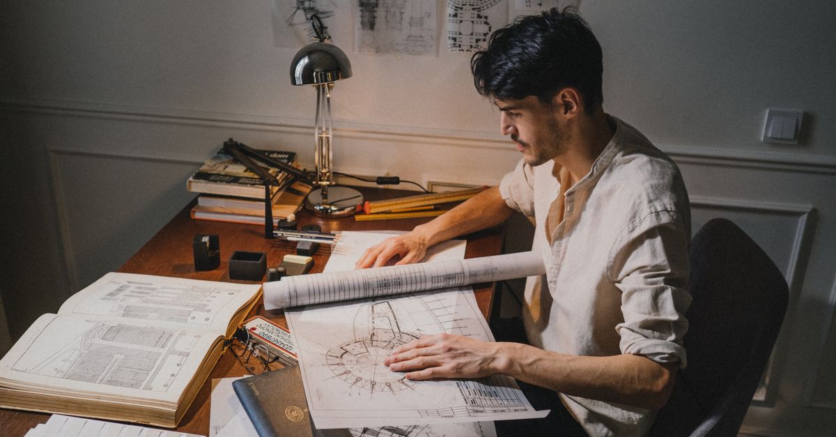 An architect working on drawings at a desk under lamplight