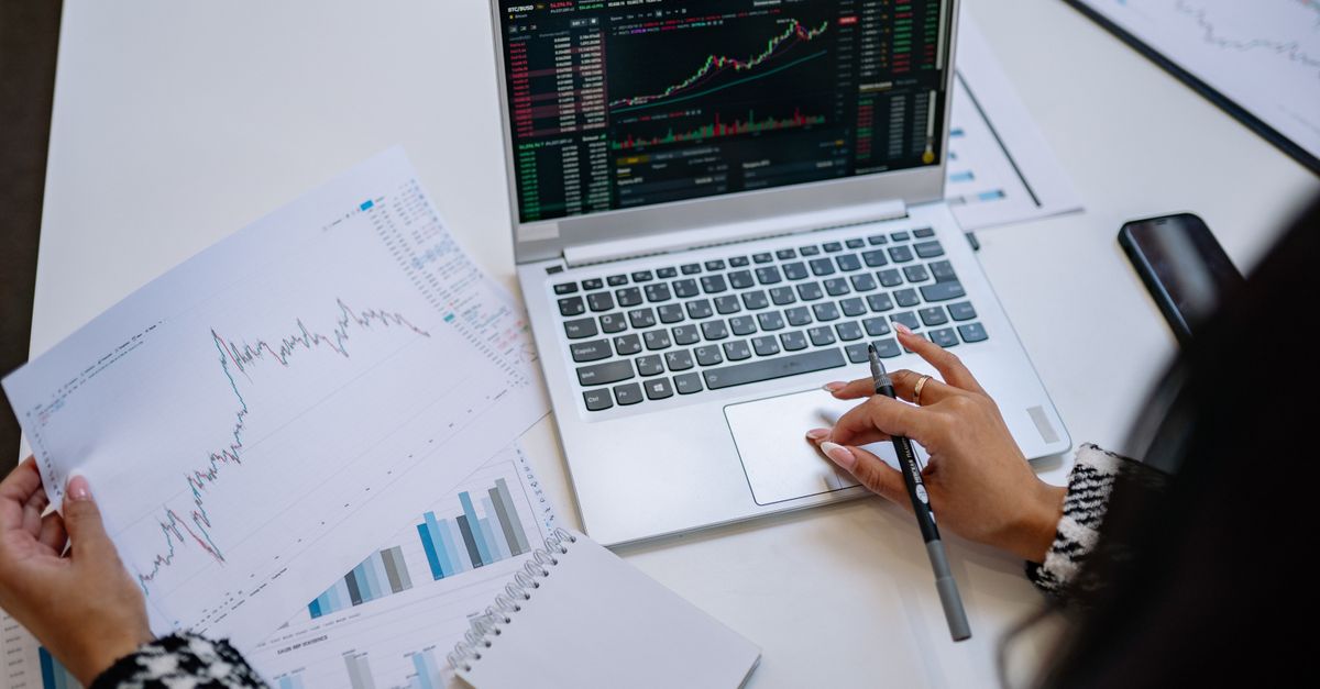A laptop showing graphs beside printed financial charts