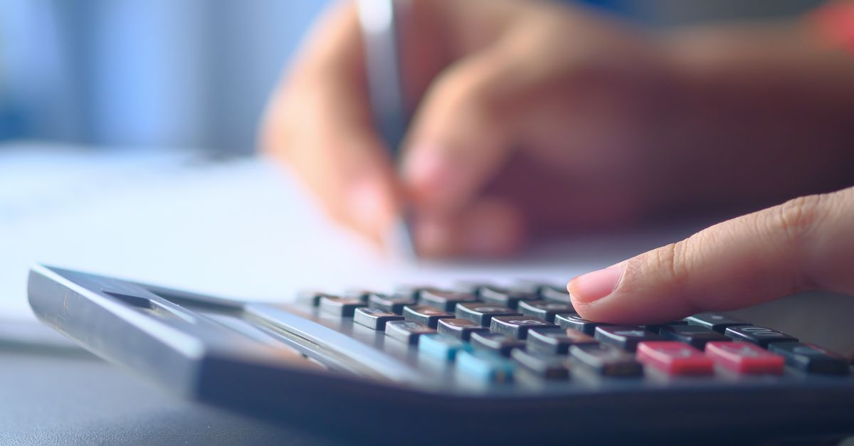 A hand writing figures next to a desk calculator