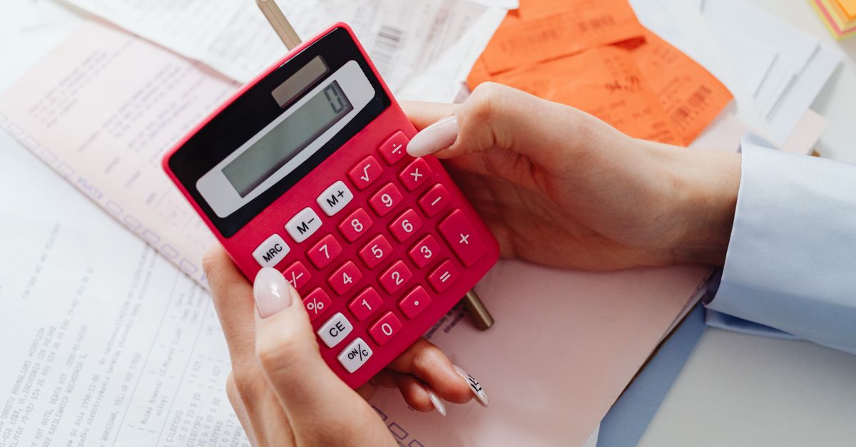 Hands holding a pink calculator over receipts and paperwork