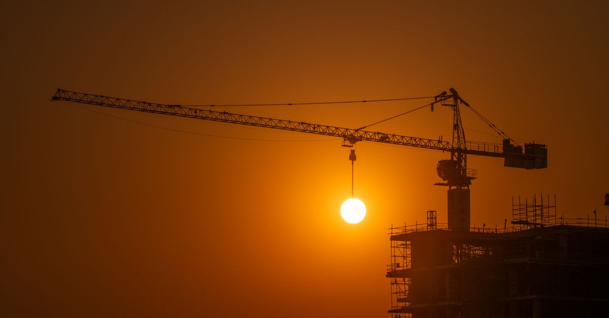 A construction crane silhouetted against a vivid sunset
