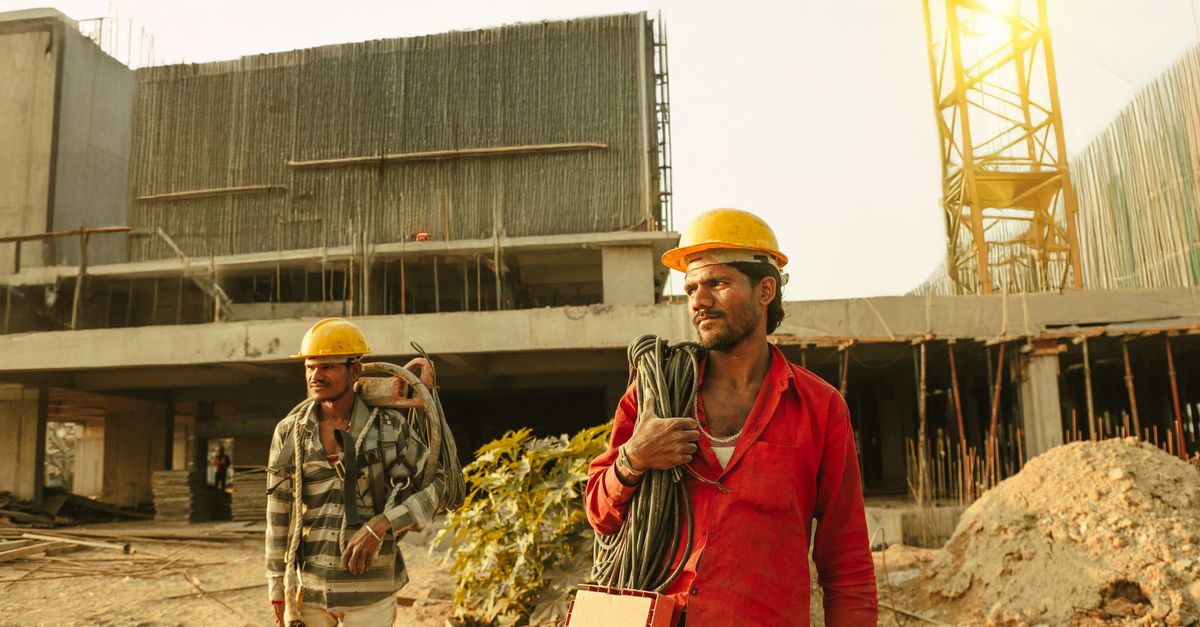 Construction workers in helmets on a building site with a crane behind them