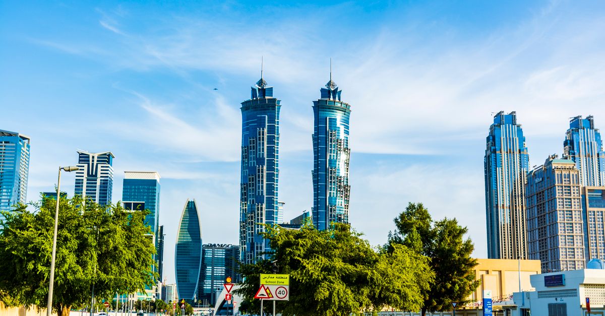 Twin residential towers and palm-lined streets in Dubai under a blue sky