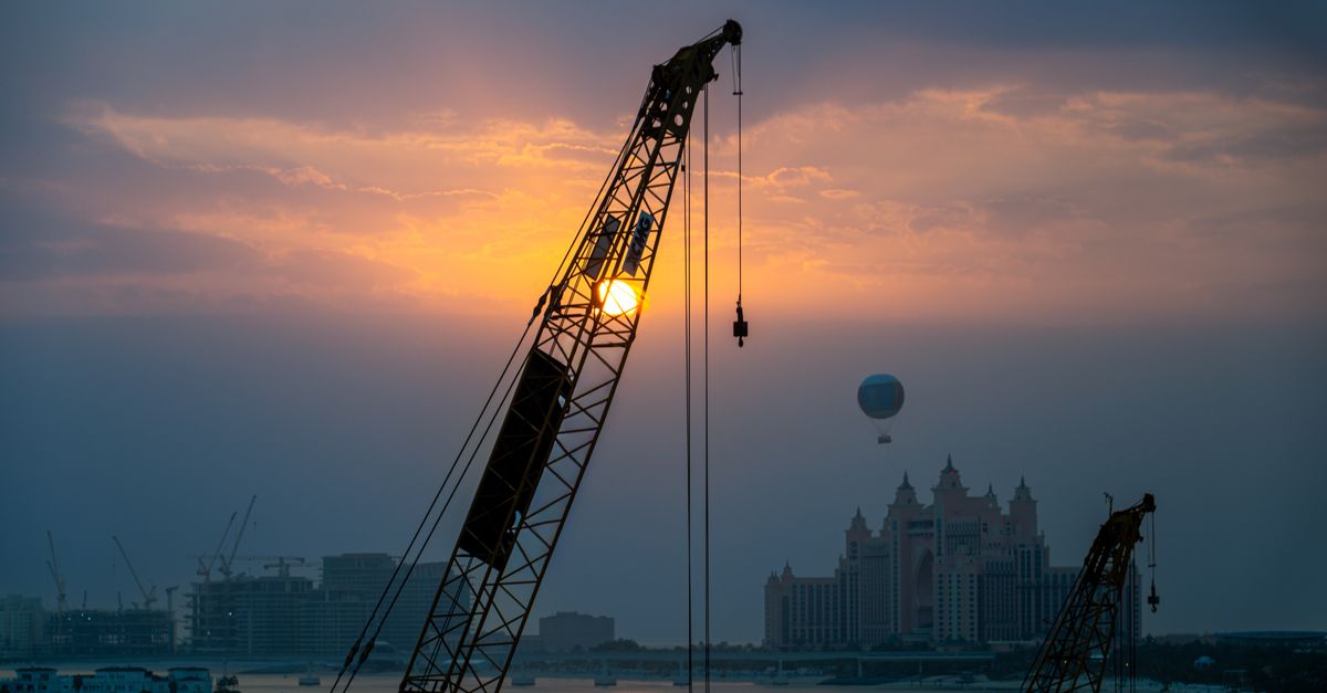 Construction cranes silhouetted against a Dubai sunset with the Atlantis hotel on the horizon