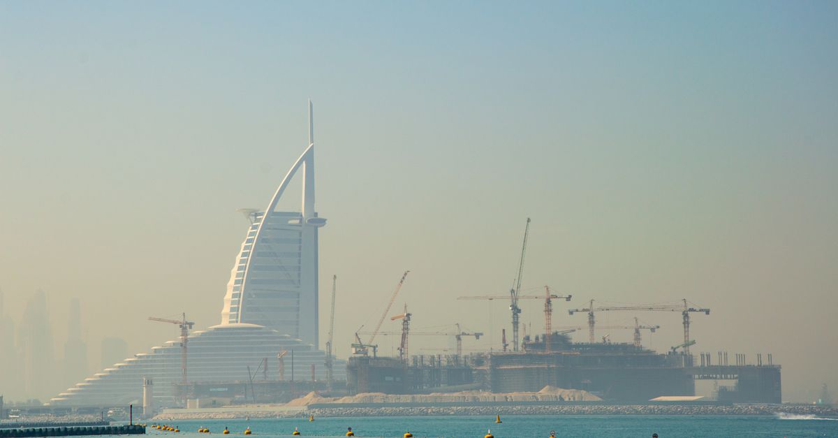 Construction cranes along the Dubai coastline with the Burj Al Arab behind