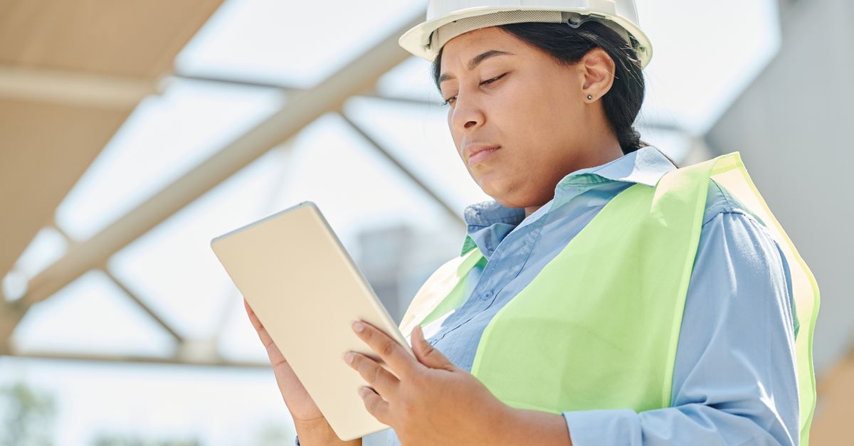 An engineer in a hard hat checking a tablet at a construction site