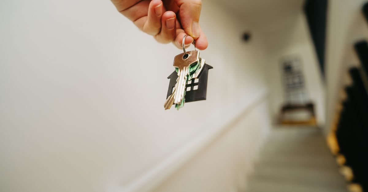 A hand holding out a set of house keys with a house-shaped key ring