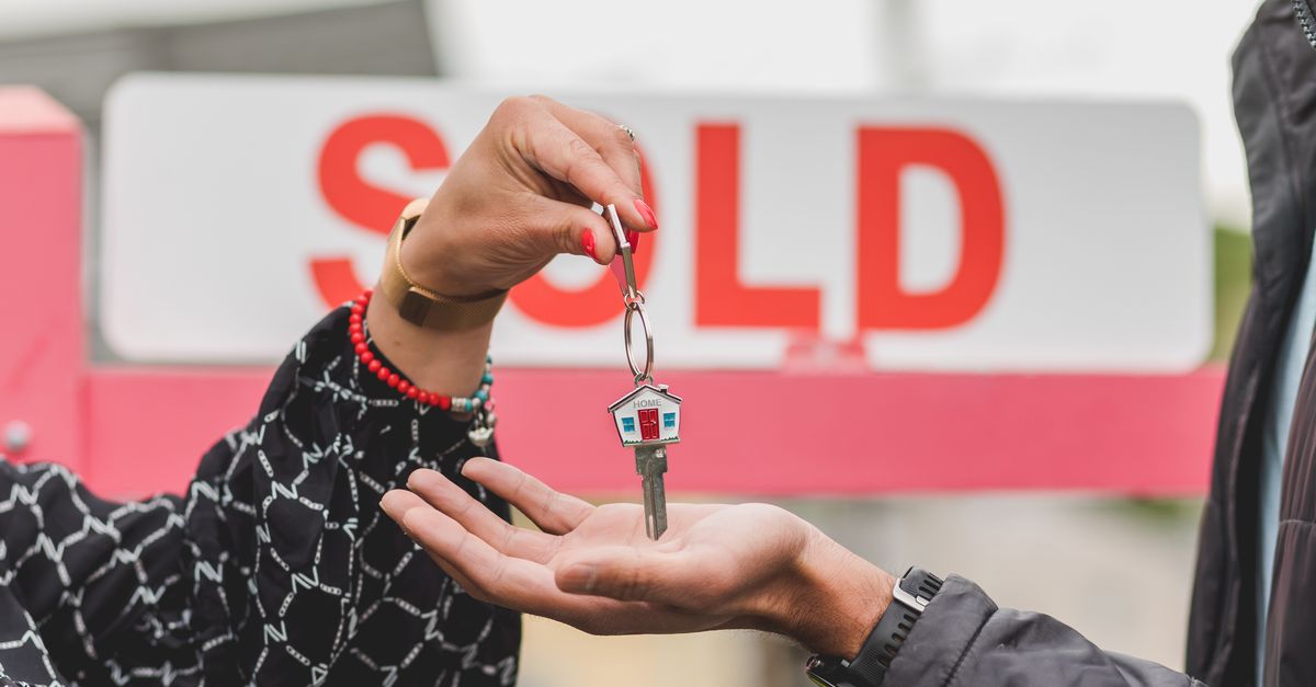 A hand passing house keys in front of a sold sign