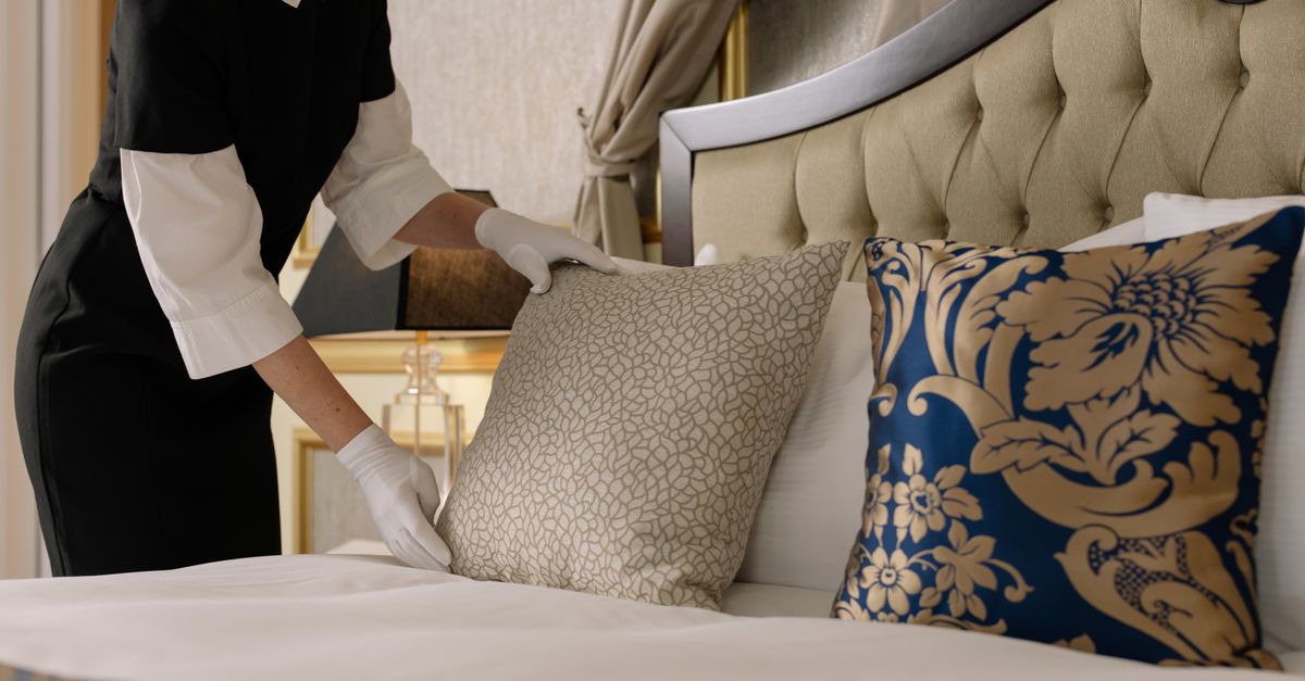 A housekeeper arranging pillows on a bed in a serviced property