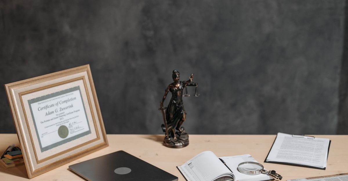 A law office desk with a statue of Lady Justice, documents and a laptop