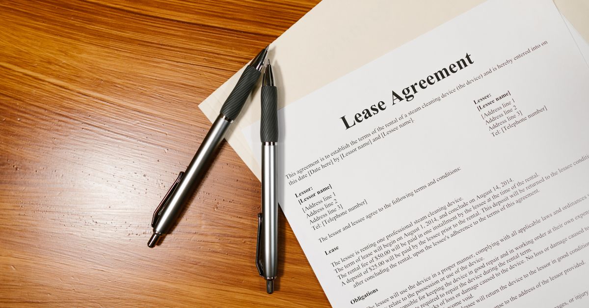 A printed lease agreement lying on a wooden desk next to two pens