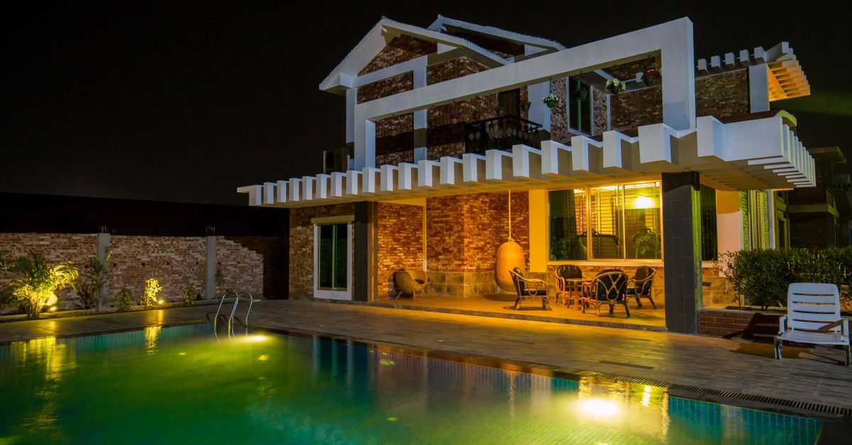 A modern house exterior with an illuminated swimming pool at night