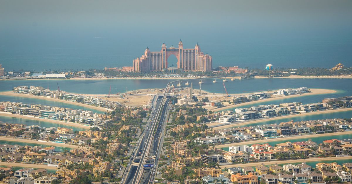 Aerial view of the Palm Jumeirah fronds lined with beachfront villas, with Atlantis in the distance