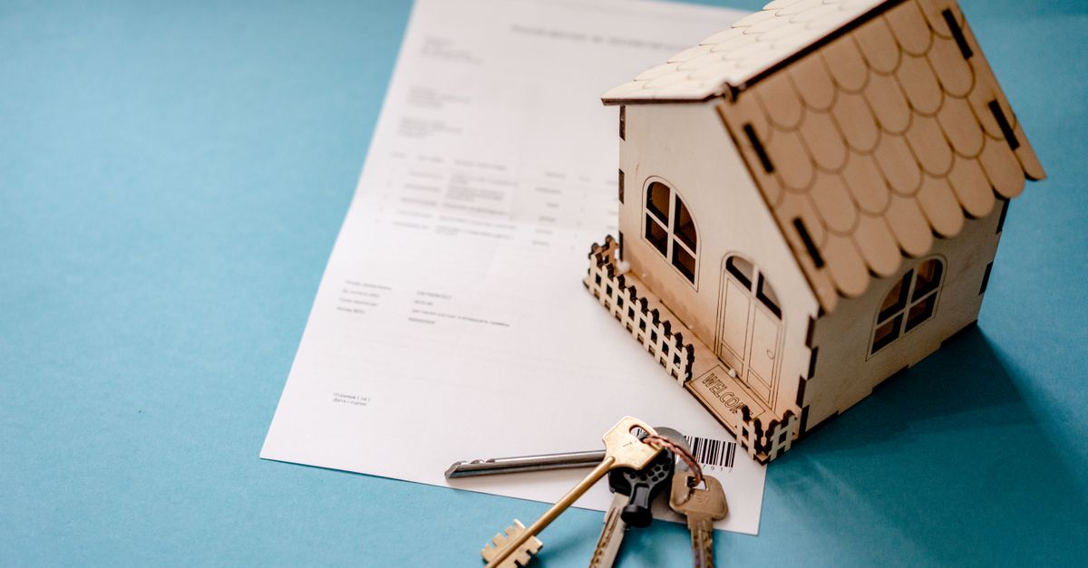 A wooden model house on top of a property contract with a set of keys