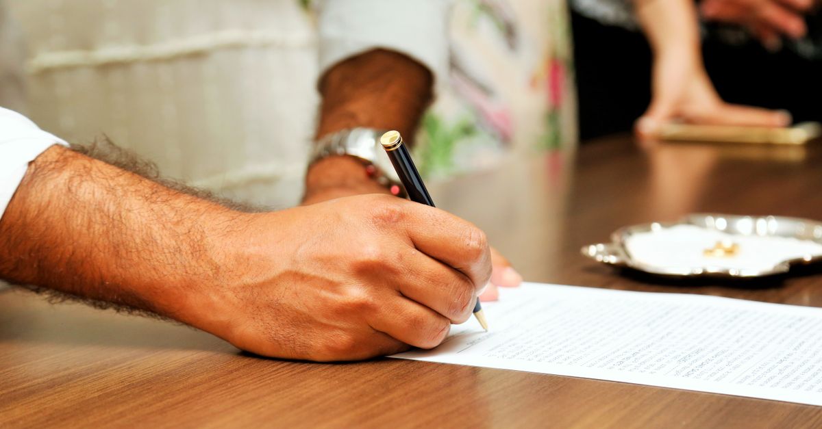 A person signing an official document with a pen at a wooden table