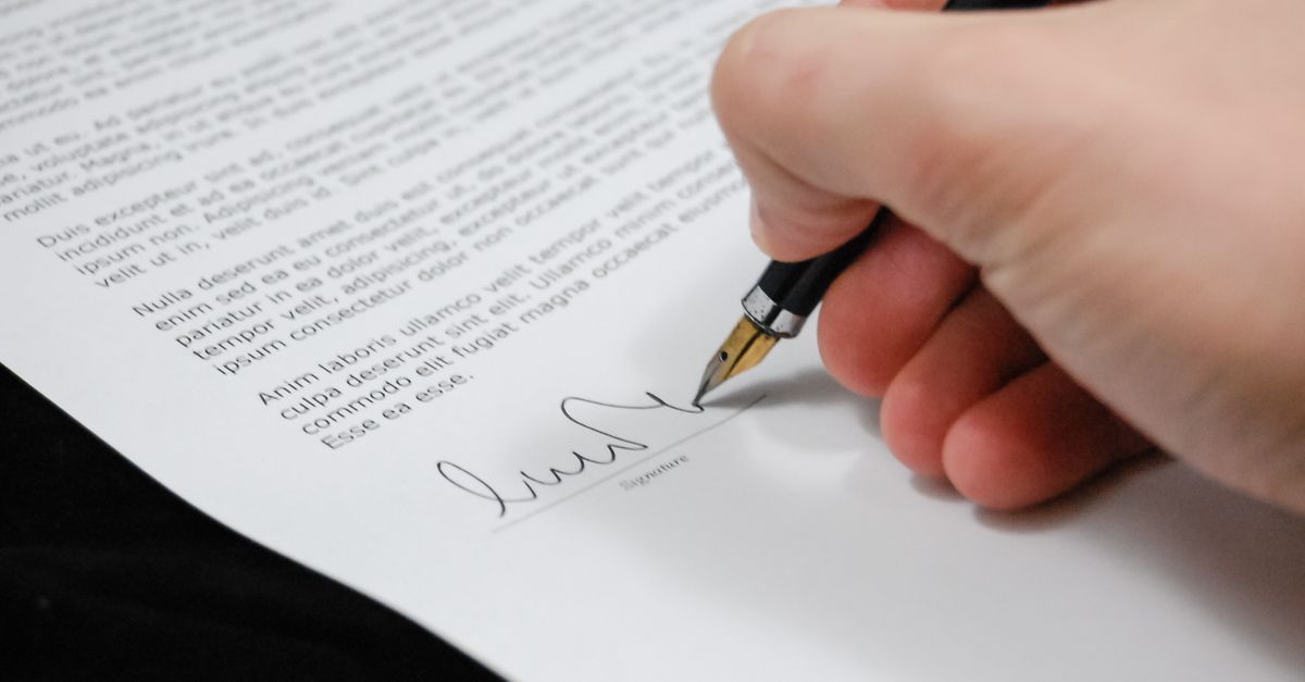 A hand signing a legal document with a fountain pen
