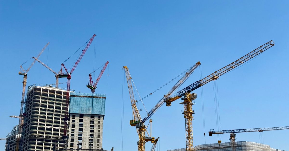 Tower cranes at a skyscraper construction site under a clear blue sky